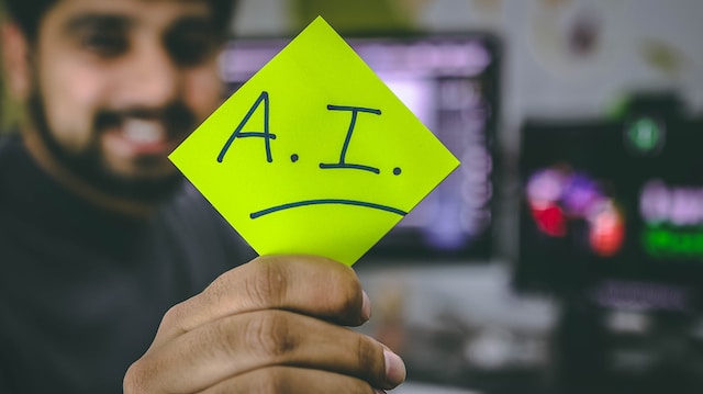 A man holdin a yellow paper where 'A.I.' written on it.